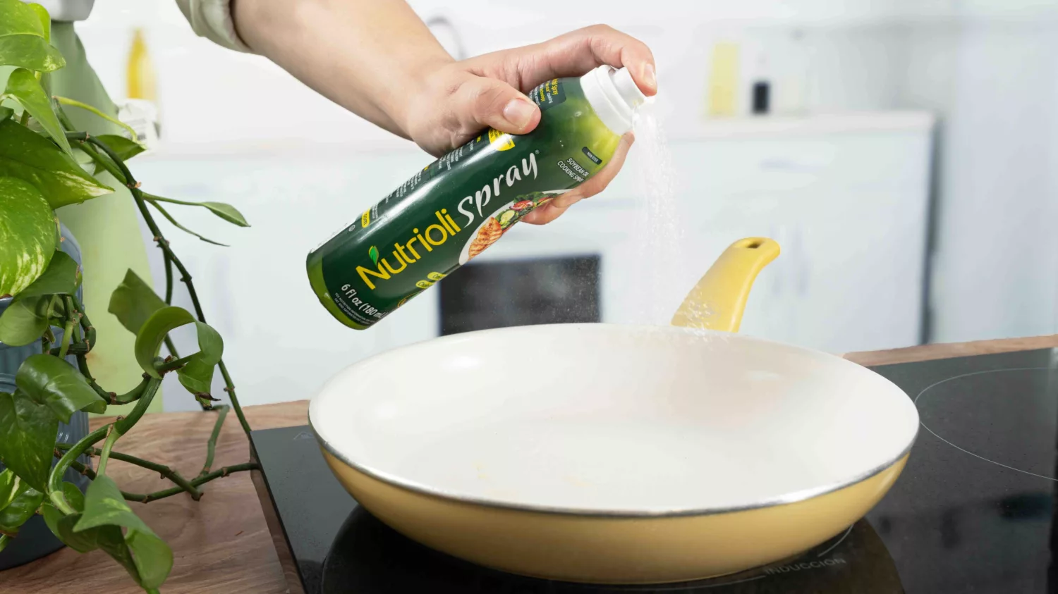 A person sprays oil spray on a frying pan